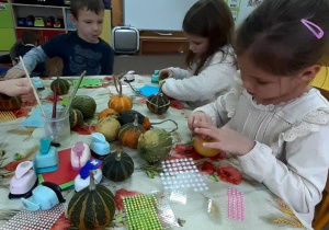 Dzieci siedzą przy stoliku i przyklejaja ozdoby na dynie